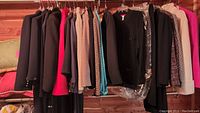 Full view of assorted women's suits, jackets, and sweaters on hangers in cedar closet with various colors including black, red, beige, and teal.