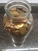 Top view of large mason jar open, showing densely packed pennies inside mostly face up and stacked horizontally and vertically.