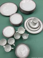 Grouped view of stacks: dinner plates, salad plates, side plates, cups and saucers on green background.