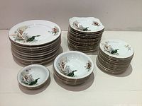 Full set of stacked vintage bone china plates and bowls with floral calla lily pattern and gilded rims.