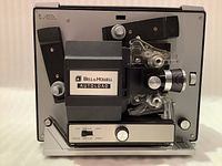 Front angled view of Bell & Howell Autoload 8mm movie projector showing the lens, film loading area, brand label, and control knobs on the base plate.
