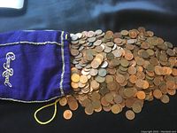 Wide shot of a large number of old Canadian pennies spilling from a purple Crown Royal bag on a black surface.