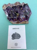 Front view of amethyst clock and accompanying Ontario Provincial Gemstone information pamphlet lying flat on turquoise background.