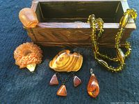 Photo showing Baltic amber necklace, amber brooch on natural wood, amber pendant, two amber hedgehogs, and hand-carved wooden chest lid open beside items