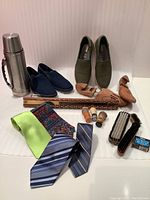 Full layout of men's shoes, wooden stretchers, tie rack with four silk ties, shoe brushes, shaving brushes, shoe polish, and thermos