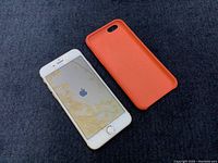 Apple iPhone 6 with screen on showing discoloration paired with separate orange silicone case.