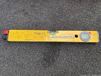 Close-up photo of the Johnson branded yellow laser level showing markings and bubble vial, with laser emitter at one end.