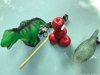 Dark green Tyrannosaurus Rex lamp, red foam apple pop art composition, and teal shark lamp together with measuring tape