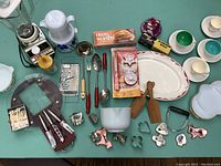 Overview showing mix of vintage and modern kitchen items including Oster blender, thermos, utensils, baking tools, cookie cutters, and teacups.