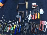 Wide view of assorted hand tools laid out including screwdrivers, pliers, hand drill, and outage meter