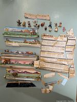 Overview of 30 hand-painted Hanna Barbera Marx Tinykins figurines laid out on a light surface, partially in original packaging with deteriorated paper backdrops.