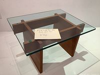 Overview of table from front-left angle showing glass top and teak base cross structure