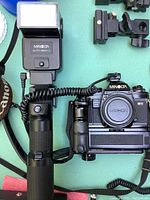 Minolta X700 camera body mounted on a motor drive, with a Minolta Auto 3600 PS flash unit attached to a handle grip, coiled cable connecting flash and camera.