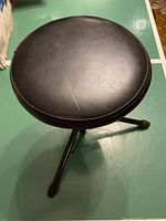 Top view of the round black padded seat of the musical stool showing slight surface wear.
