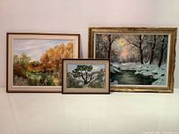 Full view of all three framed landscape oil paintings showing fall, winter, and summer scenes grouped together.