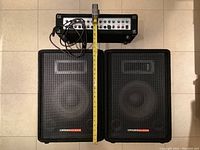 Top-down view of amplifier atop two speakers with tape measure showing combined height
