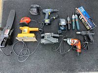 Full set of power tools laid out on a surface showing chain saw, various sanders, drills, and screwdrivers.