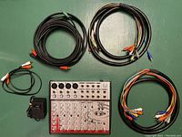 Top-down view of Pyle Pro audio mixer with power adapter and four sets of RCA audio cables spread around.