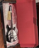 Miniature guitar replica of John Lennon’s Rickenbacker guitar laid inside a box with protective bubble wrap.