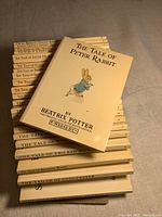 Stack of 23 vintage Beatrix Potter books laid on a surface, showing the top book 'The Tale of Peter Rabbit' with cover illustration and title.