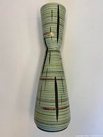 Full view of hourglass-shaped vase with textured green glaze and abstract black, red and yellow lines
