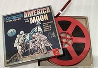 Color photo showing 'America on the Moon' Apollo 11 movie reel in original box with red film reel visible.