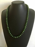 Front view of the vintage 22-inch green jade bead necklace displayed on a black bust stand, showing uniform spherical beads.