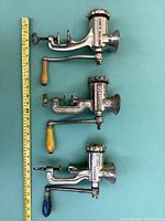 Overview photo showing three vintage heavy cast meat grinders with wooden handles and a tape measure for size reference