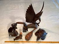 Six hand carved wood animal sculptures displayed together on fabric with ruler showing size range.