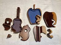 4-piece set of hand-carved wooden puzzles arranged on fabric surface showing disassembled guitar and apple shapes with multiple interlocking pieces