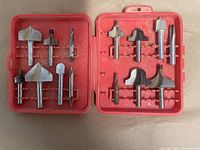 Open red plastic case showing 14 high speed steel router bits in various profiles for woodworking. The bits have 1/4 inch shanks.