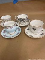 Four English bone china teacups each on matching saucers, showing different floral designs and gold accents