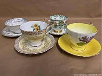 Four different English bone china teacups and matching saucers on a beige background