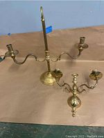 Older adjustable brass candlestick with central stem, round base, and two candle arms placed on a surface alongside the smaller brass wall sconce.