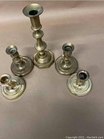 Top view of five brass candlesticks arranged showing variation in height and design.