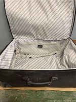 Open view of large black suitcase interior showing light striped lining and adjustable straps.