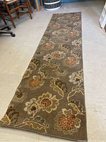 Full view of one 8 foot runner rug with floral pattern on brown background.