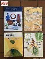 Four auction catalogues laid flat showing cover designs featuring Asian art and ceramics, including a blue vase, intricate pottery, and traditional paintings.