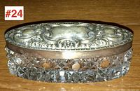 Top angled view showing ornate sterling silver lid with Edwardian floral motifs and blank cartouche center, atop cut crystal base with diamond pattern.