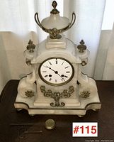 Front view showing full alabaster case, enamel dial, ormolu mounts, pendulum bob and winding key placed in front