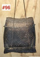 Front view of antique Burmese wicker basket showing woven wicker body, braided rim, and attached shoulder straps with carved wooden base underneath.