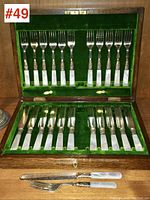 Opened mahogany box showing top and bottom trays of mother-of-pearl handled forks and knives.