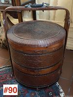 Full view of large tiered Asian basket, showing round stacked tiers and bamboo handle with brass fittings.