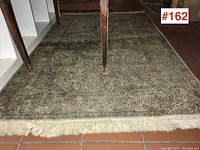 Full view of the vintage Persian carpet under a table showing the floral patterned design and fringe edge.
