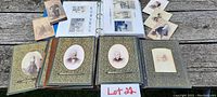 Overview of two antique photograph albums open on weathered wood surface with several loose cabinet photos placed around.