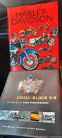 Two hardcover books in the lot, one red Harley-Davidson Model History book, and one dark Chevy Small-Block V8 book, both with illustrated covers.
