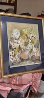 Full view of the framed floral watercolor painting showing the gold-tone frame and blue mat around the abstract flowers in soft warm hues.