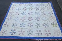 Full view of the antique quilt showing white background with colorful floral pinwheel blocks and blue border.