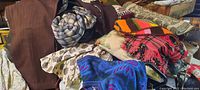 Photo showing various vintage textiles including piled clothing items, blankets, afghans, and pillows in assorted colors and patterns.