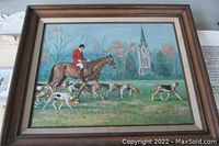 Framed oil on canvas painting showing a hunting scene with a rider on horseback and dogs, set outdoors with a church in the background.